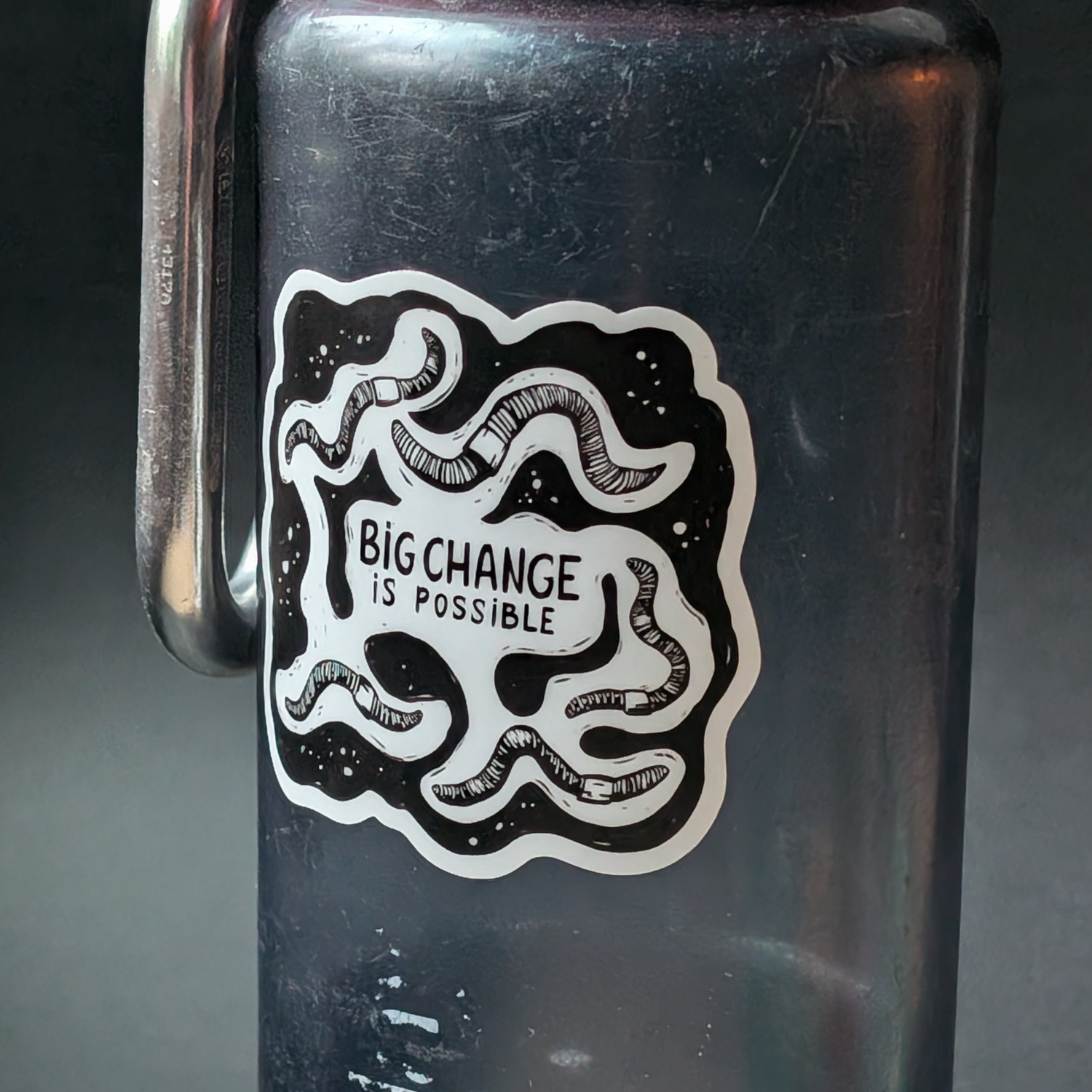 Black water bottle with 'Big Change is Possible' sticker on a dark background