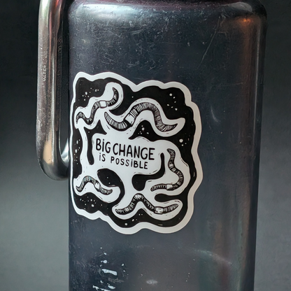 Black water bottle with 'Big Change is Possible' sticker on a dark background
